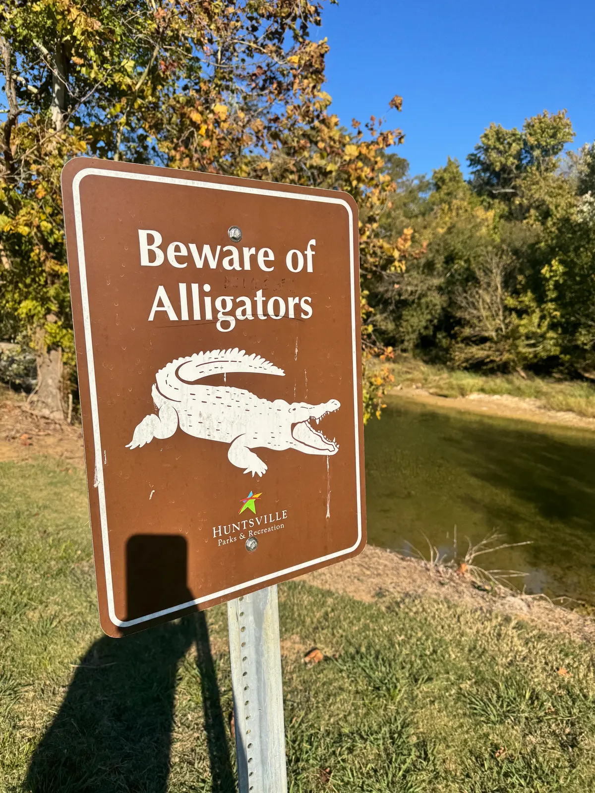A Huntsville Parks & Recreation sign reading "Beware of Alligators" beside a creek